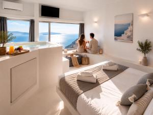 a couple sitting on a large bed in a room with large windows at Mamma Mia Santorini Suites-Volcano -Caldera -Sunset View in Fira