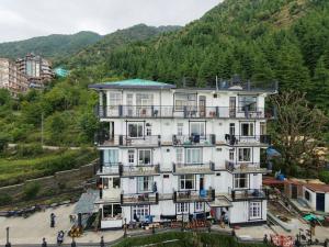 a large white building with balconies and a mountain at Oasis Guest House Bhagsu D'shala in Dharamshala