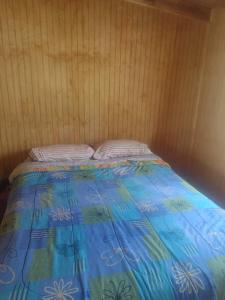 a bed with a blue comforter and two pillows at Cabaña Bellavista in Cochamó