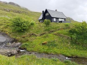 a black house on a hill next to a river at Unique and isolated cottage with stunning views in Leynar