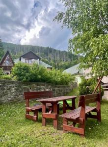 two picnic benches sitting in the grass near a stone wall at Domček u Ferka in Dedinky