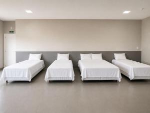three beds in a room with white sheets and pillows at HOTEL SB Butia in Butiá