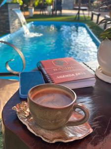 Eine Tasse Kaffee und ein Buch auf einem Tisch neben einem Pool in der Unterkunft Hotel Suites Bambú in Minga Guazú