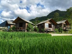 a group of wooden huts and a field of grass at De Mont Retreat Sapa in Sapa