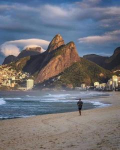 a man walking on a beach with mountains in the background at BeM Ipanema in Rio de Janeiro