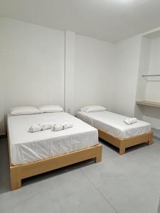 two beds in a room with white walls at Hotel Jemara in San Gil