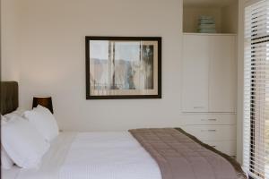 a white bedroom with a bed and a picture on the wall at Dune View Accommodation in Mangawhai