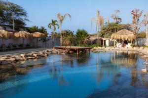 a pool of water with a picnic table and straw umbrellas at ÓRGANOS BEACH bungalows & suites in Los Órganos