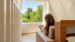 a woman sitting on a couch with a laptop in front of a window at Hongcheon Opera Bien Glamping in Hongcheon