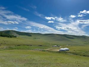 a large green field with two buildings and mountains at Batzaya Herder Camp in Ulaanbaatar +11 photos