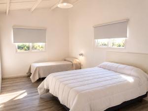 a white bedroom with two beds and two windows at Alta Vista in Villa Yacanto
