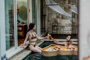 a man and a woman sitting in a swimming pool at Aksari Villa Seminyak by Ini Vie Hospitality in Seminyak