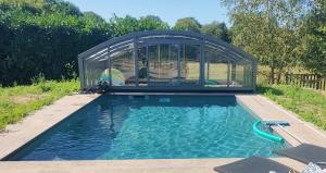 a swimming pool with a greenhouse behind it at Gîte L'Orée des Bois in Paimpont