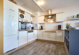 a kitchen with white cabinets and wooden floors at Haus Schildt, FeWo 8 in Duhnen