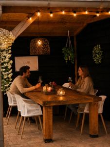 a man and woman sitting at a wooden table with wine glasses at Chalet Aan de rand - Veluwe - met sauna in Putten