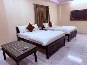 two beds in a room with a table and a tv at Sterlinge Homestay in Visakhapatnam