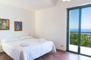 a white bedroom with a bed and a large window at Cresta Panoramic apartments in Naso