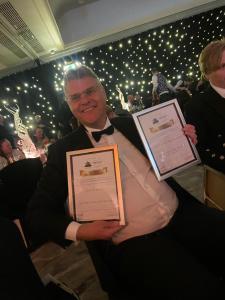 a man in a tuxedo holding two certificates at Lime Tree Hotel in Fort William