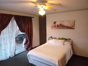 a bedroom with a bed with a ceiling fan and a window at Afro Rasta Kumusha in Germiston