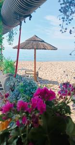 a beach with a straw umbrella and some flowers at Barrosu Studio Apartment in Orosei