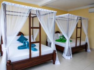 two beds in a room with white drapes at Tumaini Bungalows in Nungwi