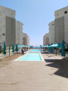 a swimming pool with blue umbrellas and chairs at Résidence Costa in Sousse
