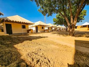 a group of cottages with trees and a dirt road at Quba Desert Camp Jaisalmer in Jaisalmer