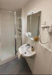 a white bathroom with a sink and a shower at Hotel Restaurant El Greco bei der Taffingsmühle in Saarlouis