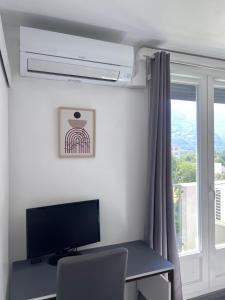 a room with a desk with a television and a window at La Pinéa 40 m2 T2 climatisation, tram E et parking in Saint-Égrève