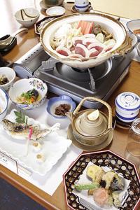 a table with plates of food and a pot on a stove at Minshuku Ryokan Kawai in Shinshiro