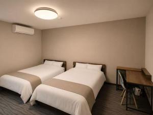 two beds in a hotel room with a desk at White Chalet Niseko in Niseko