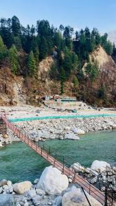 a bridge over a river with rocks and trees at Mahi camping in Jagatsukh