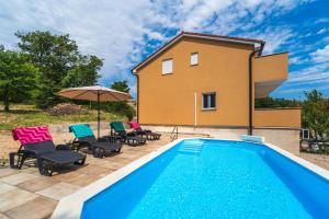 a pool in front of a house with chairs and an umbrella at Holiday house Gloria in Vrbnik