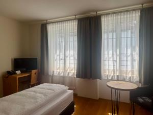 a bedroom with a bed and a table and windows at Hotel Alpenstadt in Chur