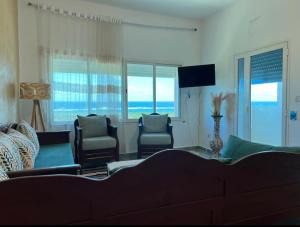 a living room with a couch and chairs and windows at Maison pieds dans l'eau in Chebba