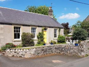 a stone house with a stone wall and a yellow door at Cloud Cottage in Duns
