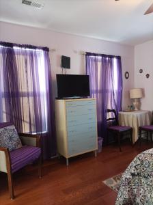 a bedroom with a dresser with a tv and purple curtains at Cantuta Inn in Harpers Ferry