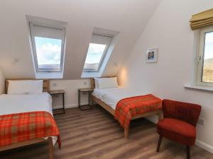 a room with two beds and a chair and two windows at 8B Carrigreich in Tarbert