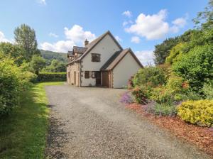 a house on a gravel road with bushes and flowers at Byne Brook Cottage in Wistanstow