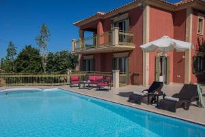 a house with a swimming pool with chairs and an umbrella at Lourdas Beach View by Villa Select in Lourdata