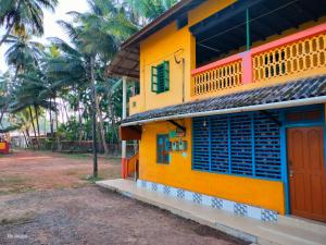a yellow building with blue windows and palm trees at Totadamane in murdeshwar in Māvalli