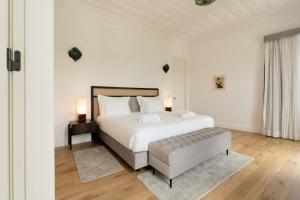 a white bedroom with a large bed and a stool at Oca Grande Hotel Do Pezo in Melgaço