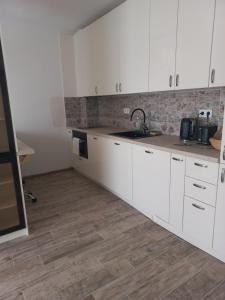 a kitchen with white cabinets and a wooden floor at Рока Резиденс in Ravda