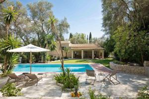 a house with a swimming pool with chairs and an umbrella at Apelia Estate - Among Ancient Olives, Experience the Quiet Soul of Corfu in Corfu