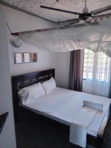 a bedroom with a bed with white sheets and a ceiling at TN Apartments deviat in Diani Beach
