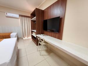 a hotel room with a desk with a tv on a wall at Spazzio diRoma Caldas Novas in Caldas Novas