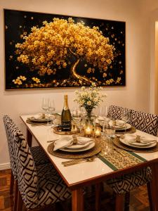 a dining room table with chairs and a painting of a tree at Roupa cama Wi-Fi garagem ar Cond beira mar 50 m in Tramandaí +16 photos
