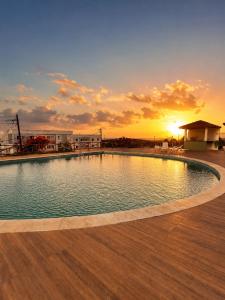 a large swimming pool with a sunset in the background at Apartamento Flores do Bosque in Garanhuns