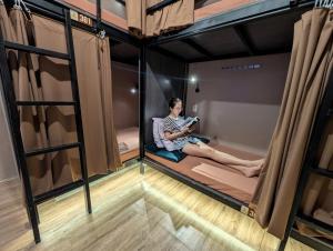 a woman is sitting on a bed in a room at T Zone Hostel - Quiet Place, Near China Town,Ho Thi Ky Street Food,Cafe,Beer in Ho Chi Minh City