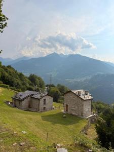 two stone buildings on a hill with mountains in the background at Arzo Mountain Chalet in Morbegno